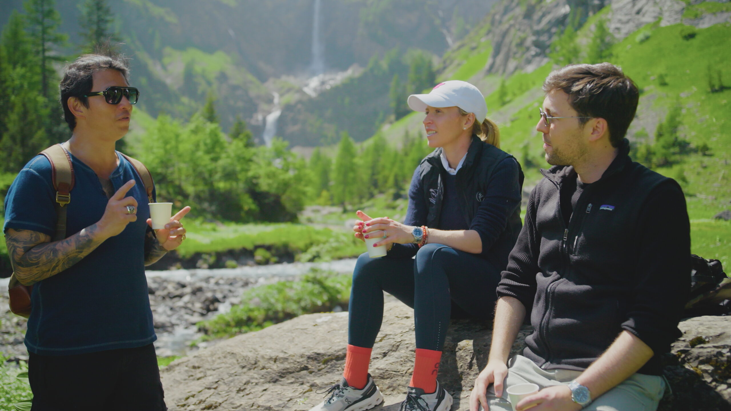Wei Koh talking with Caroline-Marie and Karl-Fritz Scheufele during a hike in Gstaad, surrounded by alpine scenery and waterfalls