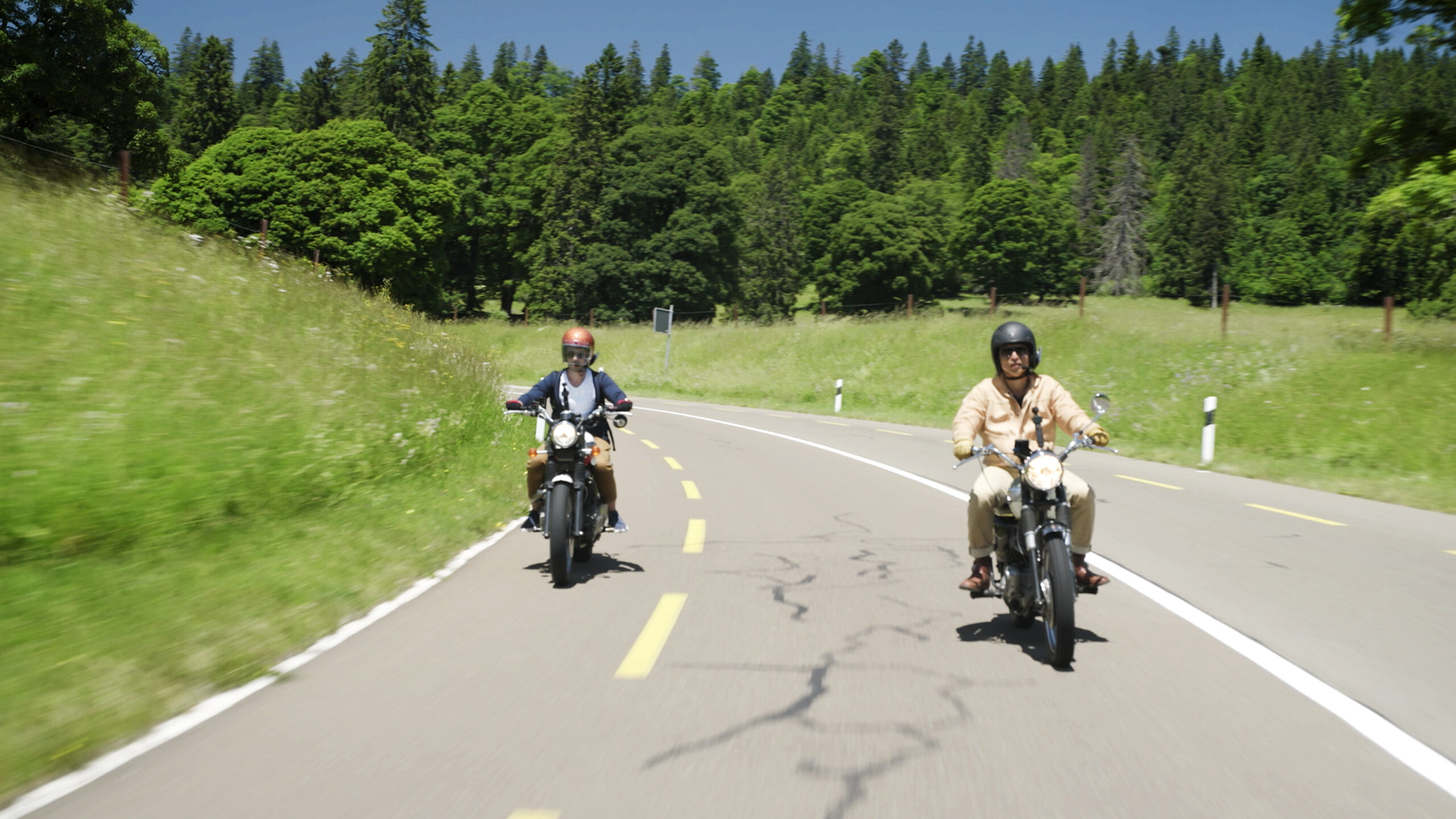 Wei Koh and Michel Nydegger riding motorcycles side by side on a winding country road in Switzerland while filming the Greubel Forsey episode of Man of the Hour